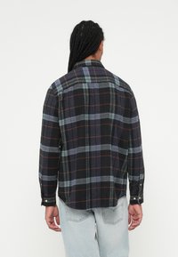 Sort flannel skjorte med blå, grå og orange ternet mønster. Lange ærmer med knapmanchetter og en afslappet pasform. Bomuldsstruktur, kravedetaljer.