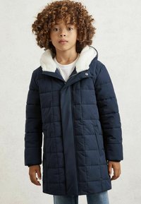 Mornarska puhovka z belo flis podloženo kapuco, prešita zasnova, sprednji zadrga in stranske žepe. Oblečeno nad belo srajco in jeans hlačami.