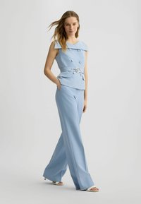 Helles blaues, maßgeschneidertes Anzug-Outfit mit weit geschnittenen Hosen und einer taillierten Bluse mit schulterfreiem Design und zwei großen Knöpfen. Silberner Gürtel inklusive.