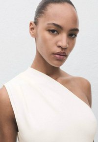 Vestito asimmetrico bianco sporco con una spalla, realizzato in un tessuto liscio. Il design aderente esalta il décolleté e la clavicola.