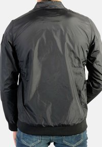 Sort nylon bomberjakke med en glat tekstur, ribstrikkede ærmeender og kant, samt et enkelt design. Har en rygkrave og ingen synlige detaljer.