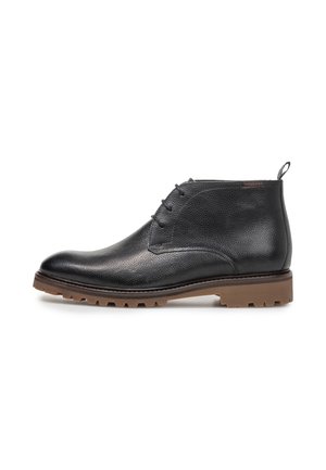 Stivaletto nero in pelle con allacciatura frontale e suola in gomma marrone con carrarmato, mostrato di profilo su sfondo bianco.