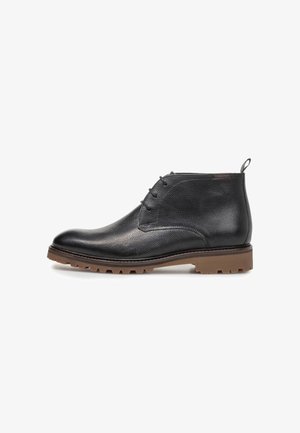 Stivaletto nero in pelle con allacciatura frontale e suola in gomma marrone con carrarmato, mostrato di profilo su sfondo bianco.