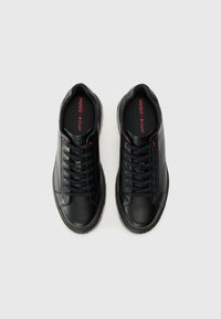 Black leather sneakers with textured toe caps, lace-up design, red accents, and black padded collar. Sole features a slight tread pattern.