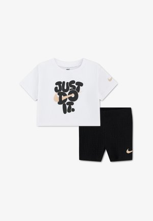 Balti trumpa Nike marškinėlių su užrašu „Just Do It“ ir smėlio spalvos logotipu, derinama su juodais tekstūruotais šortais, kuriuose yra smėlio spalvos Nike logotipas.