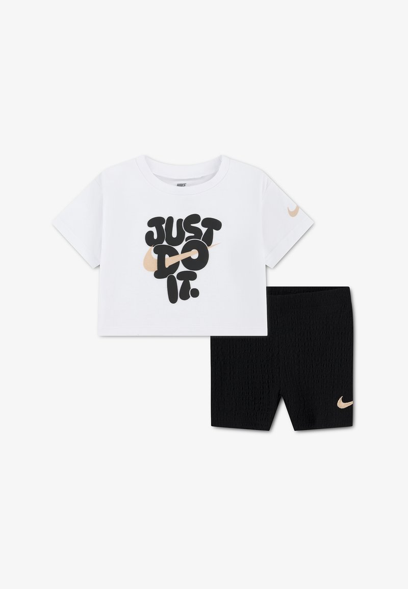 Λευκό κοντό t-shirt της Nike με το κείμενο «Just Do It» και μπεζ λογότυπο Swoosh, σε συνδυασμό με μαύρα υφασμάτινα σορτς με μπεζ λογότυπο Nike Swoosh.