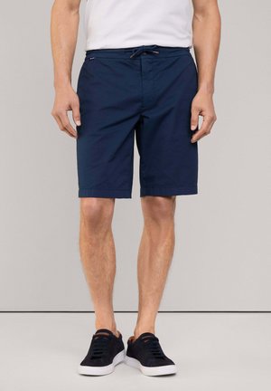 Marineblauwe shorts van lichtgewicht stof, met een trekkoord in de taille en opgerolde mouwen, gecombineerd met donkere sneakers.