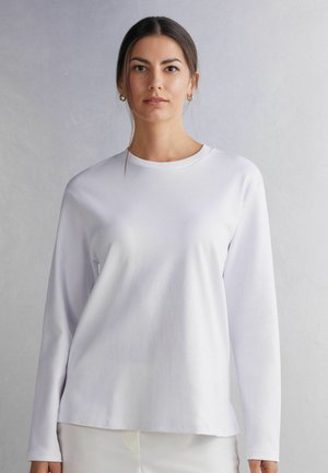 Witte langspanige shirt gemaakt van gladde stof met een ronde hals, voorzien van een relaxte pasvorm en een licht afgeronde onderkant.
