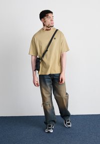 Krém színű, túlnyúló póló kis logóval, megviselt kék farmernadrág, frayed hem-mel, fekete crossbody táska, és szürke sportcipő színes kiegészítőkkel.