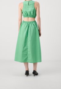 Conjunto de dos piezas verde que presenta un top corto con banda elástica y una falda larga y fluida. Textura suave con un ajuste relajado y cierre en la parte posterior.