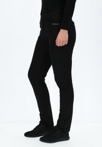 Zwarte slim fit broek gemaakt van een gladde, rekbare stof. Heeft een platte voorkant, zijzakken en een effen tailleband. Gepaard met zwarte sneakers.