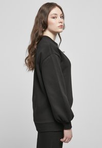 Felpa nera con vestibilità comoda, maniche larghe e polsini a coste. Texture liscia, design a girocollo e colore uniforme.