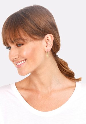 Boucles d'oreilles pendantes en forme de note de musique en ton doré avec un design à crochet. Légères avec un motif délicat et intriqué.
