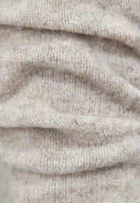 Tissu tricoté beige clair avec une texture douce et duveteuse, présentant un motif côtelé et un tombé délicat, indiquant élasticité et chaleur.