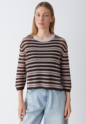 Woman wearing a brown and light pink striped knit sweater with three-quarter sleeves and light blue high-waisted jeans.