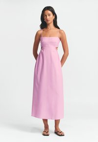 Rosa linne maxi-klänning med spagettiband, utskurna sidor och rak halsringning, med en slät textur och minimalistisk design.