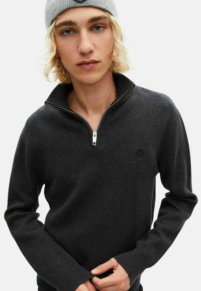 Donkergrijze zip-up trui van zacht materiaal, met een hoge kraag en geribde manchetten. Een klein logo is op de borst geborduurd.