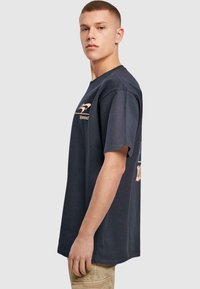 Tricou scurt, de culoare albastră închis, din bumbac, cu un logo grafic de culoare portocalie deschisă pe piept și pe spate. Design cu croială dreaptă.