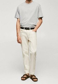 T-shirt in cotone grigio, pantaloni in denim bianchi, cintura nera e sandali marroni. Design minimalista con una vestibilità comoda e una texture leggera.