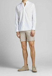 Valkoinen nappikauluspaita, jossa on pieniä monivärisiä pisteitä, beige pellavashortsit ja vaaleanharmaat nauhalliset kengät. Yksinkertainen ja rento muotoilu.