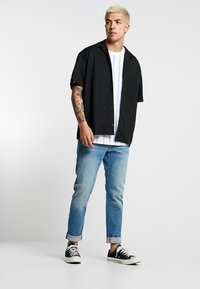 Black short-sleeve shirt with a pocket, white striped undershirt, light blue jeans, and black shoes with white soles. Simple, casual outfit.