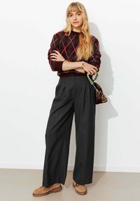 Pull à losanges bordeaux, pantalon large sombre, et chaussures à enfiler beige avec semelles marron. Accessoires comprenant un sac à main imprimé léopard.