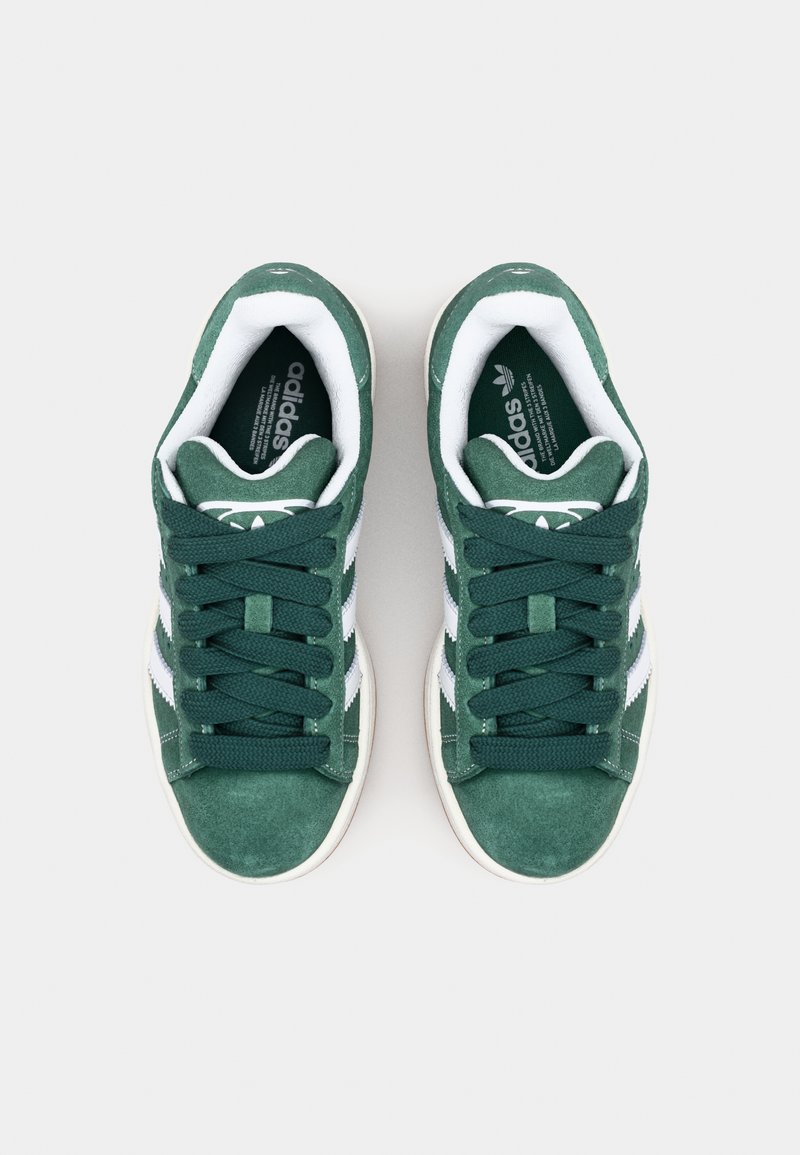 Grüne Wildledersneaker mit weißen Streifen und Schnürsenkeln. Sie verfügen über eine strukturierte Oberseite und einen gepolsterten Kragen für zusätzlichen Komfort. Flache Gummisohle.