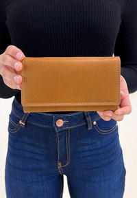 Tan leren portefeuille met een gladde textuur en zichtbare stiksels, in handen gehouden. Heeft een rechthoekige vorm en een eenvoudig ontwerp.