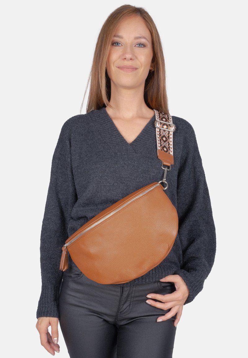 Sac bandoulière en cuir marron de forme arrondie, fermeture éclair argentée et bandoulière à motif. Le sac présente une surface texturée et un détail de frange.