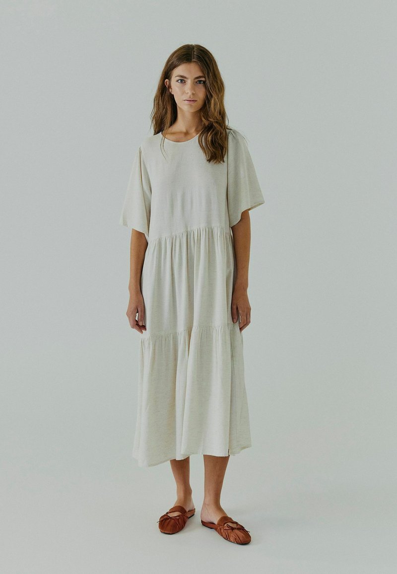 Robe beige clair, longueur genou, à manches courtes, design à volants, texture douce, assortie à des chaussures marron à enfiler avec un détail de nœud.