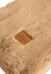 Tessuto in faux fur color tan con una morbida texture, caratterizzato da una toppa quadrata in pelle marrone goffrata con un logo geometrico.