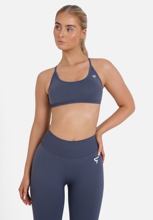 Top sportivo grigio con spalline sottili, tessuto strutturato e dettaglio del logo, abbinato a leggings grigi a vita alta con finitura liscia.