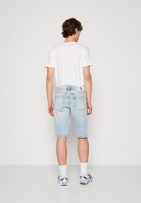 Shorts di denim blu chiaro con taglio dritto, etichetta di marca sul retro, abbinati a una maglietta bianca semplice e calze sportive bianche.
