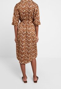 Bruine jurk met patroon, een kraag, korte mouwen en een ceintuur in de taille. De textuur is geribbeld met een golvend ontwerp.