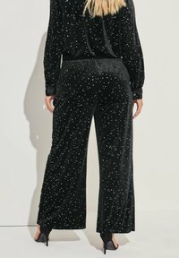 Svarta sammetsbyxor med en avslappnad passform, prydda med ett spritt stjärnmönster i silver. Midjan är elastisk och har en slät yta.