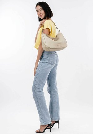Borsa hobo color crema con superficie testurizzata, accessori in argento e forma curva. Il modello indossa un top giallo, jeans blu e tacchi neri.