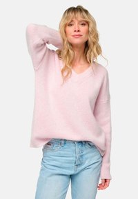 Pull en v rose clair en tissu doux et texturé, coupe décontractée avec manches longues, assorti à un jean bleu clair.
