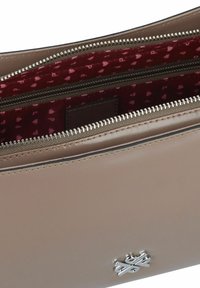 Pochette en cuir beige avec une texture lisse, quincaillerie en argent et un intérieur bordeaux présentant un petit motif en forme de cœur. Fermeture zippée.