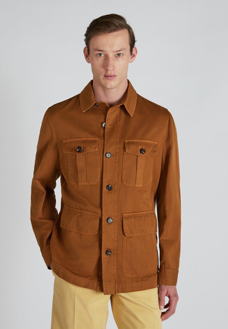 Chaqueta de algodón marrón con cierre de botones, dos bolsillos en el pecho y dos bolsillos inferiores. Presenta un cuello con solapa y una tela texturizada.