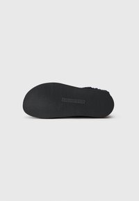 Suela de zapato de goma negra con surcos texturizados, con un logotipo estampado en el centro. Diseño plano adecuado para uso casual.