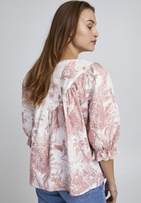 Lettet bluse med blomsterprint i rosa og hvid. Har pufærmer, en flæsekant og en rund krave.