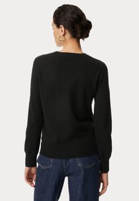 Czarny sweter wykonany z miękkiego materiału, z długimi rękawami, okrągłym dekoltem i ściągaczami na mankietach. Noszony na niebieskich dżinsach, prezentujący luźny krój.