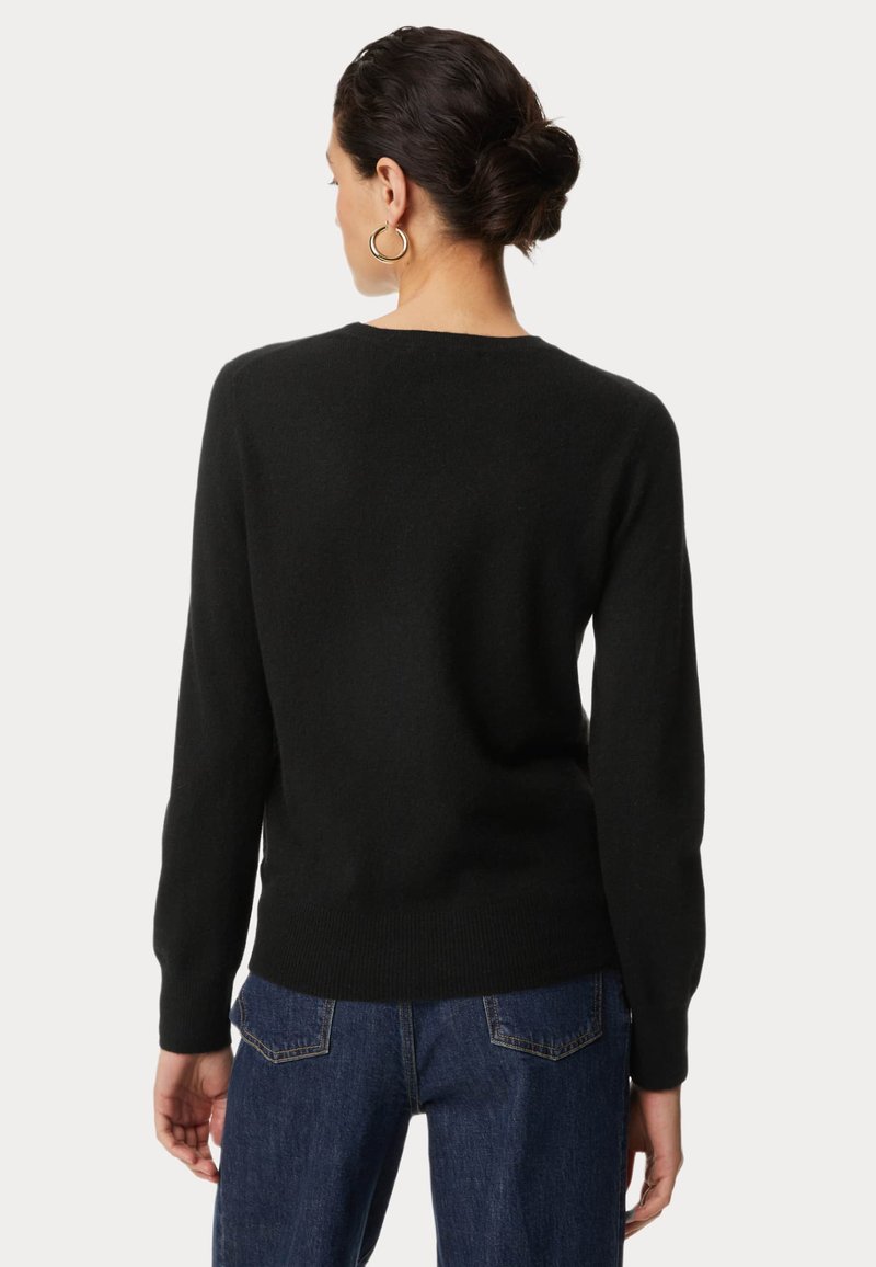 Czarny sweter wykonany z miękkiego materiału, z długimi rękawami, okrągłym dekoltem i ściągaczami na mankietach. Noszony na niebieskich dżinsach, prezentujący luźny krój.