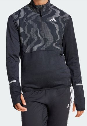 Person wearing black long-sleeve sports top with reflective abstract pattern and thumb holes, paired with black athletic pants with white stripes.