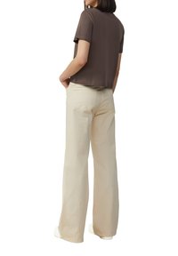 Haut marron à manches courtes avec une coupe droite, associé à un pantalon large beige pâle. La tenue présente une coupe décontractée et des poches à l'arrière.