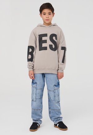Felpa grigia con testo nero "BEST", abbinata a jeans cargo blu chiaro caratterizzati da molteplici tasche e una vestibilità rilassata. Le sneakers nere completano il look.