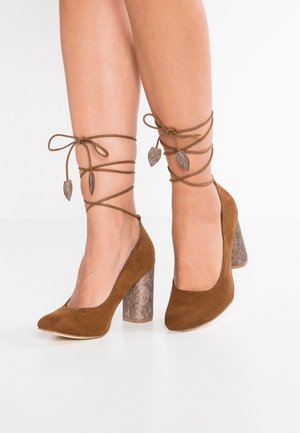 Bruine suède hoge hakken met een gestructureerde slangpatroon blokhak, met decoratieve veters rondom de enkel en bladvormige accenten.