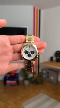 Gold metal wristwatch with a round white face, blue subdials, and a linked bracelet. Features a distinctive octagonal bezel and pushers.