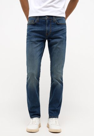 Blauwe denim jeans met een slim fit, vervagingdetails op de bovenbenen, vijf-pocketontwerp en oranje stiksel. Gecombineerd met witte sneakers.