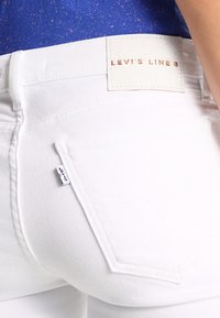 Los pantalones vaqueros blancos de mezclilla cuentan con un bolsillo trasero visible y una etiqueta de estilo cuero con el texto "LEV'S LINE 8". La tela tiene una textura suave.